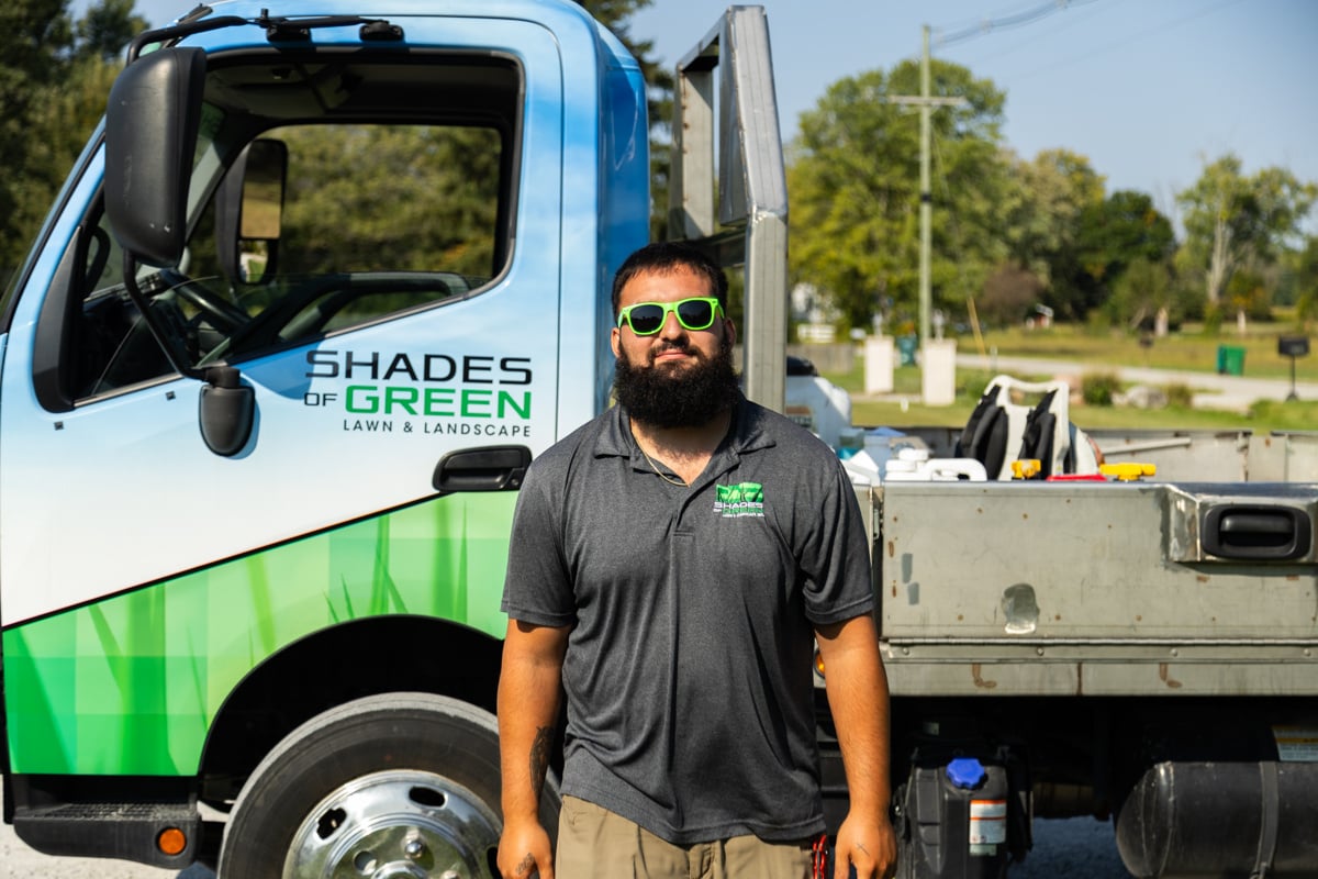 shades of green technician smiling in front of a truck