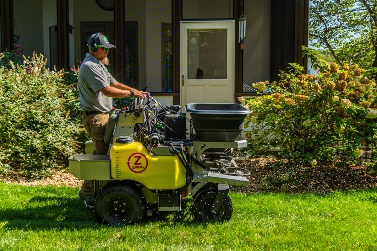lawn care technician applying fertilizer treatment to lawn