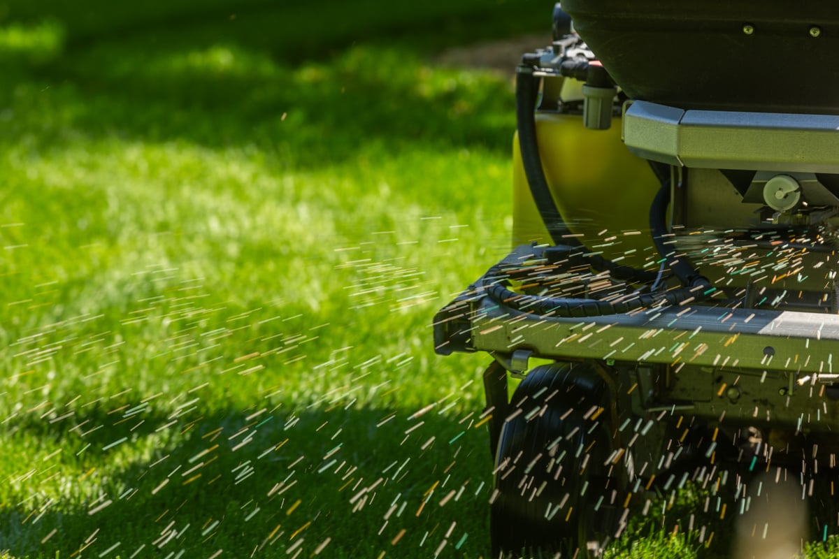 close up of slow-release granular fertilizer being applied onto grass out of a hopper