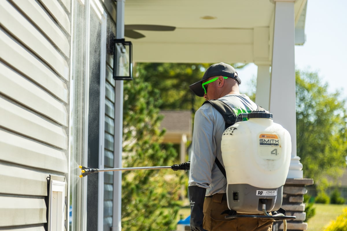perimeter pest control technician applying a seasonal treatment to prevent spiders