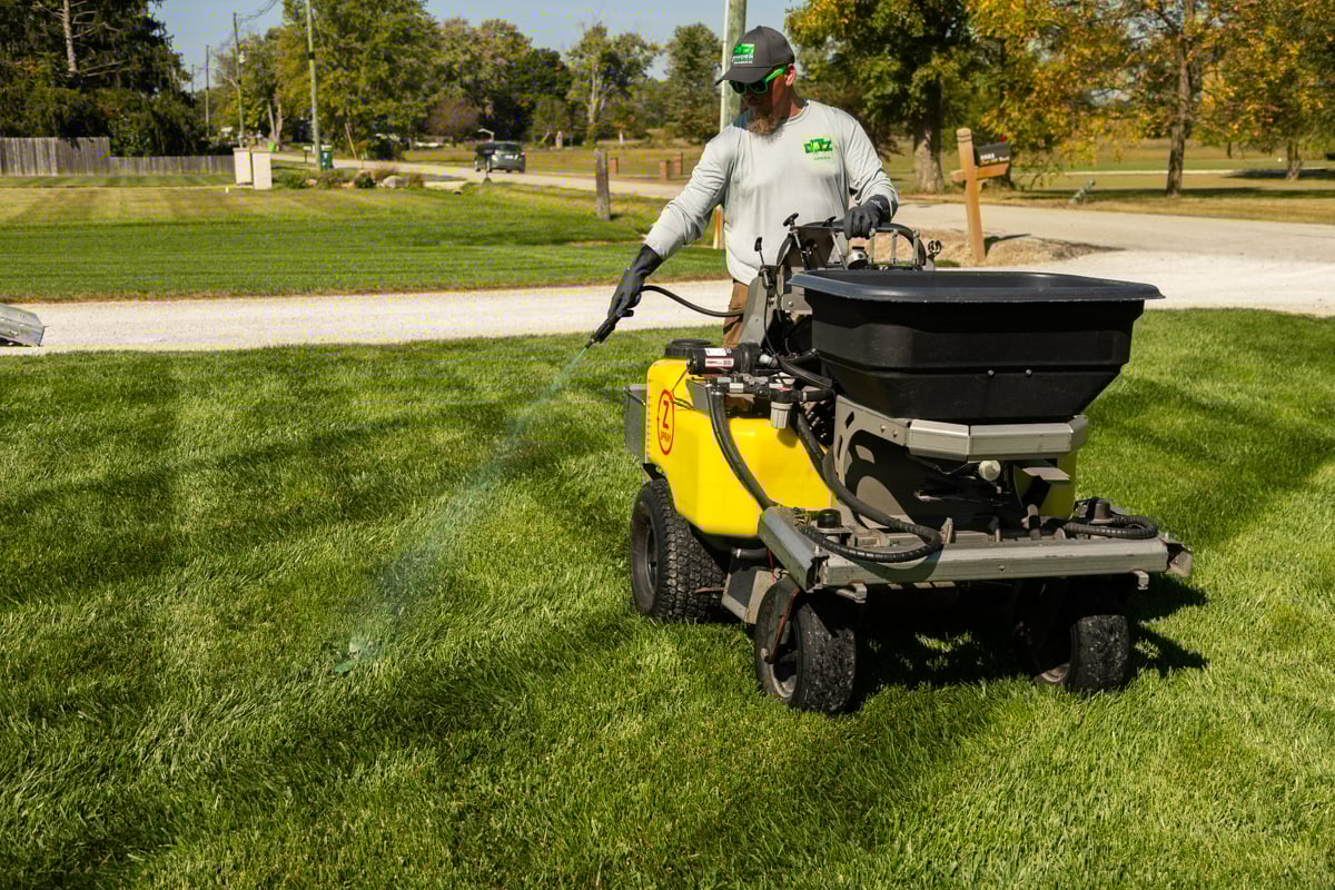 lawn care tech spot spraying a weed in grass lawn